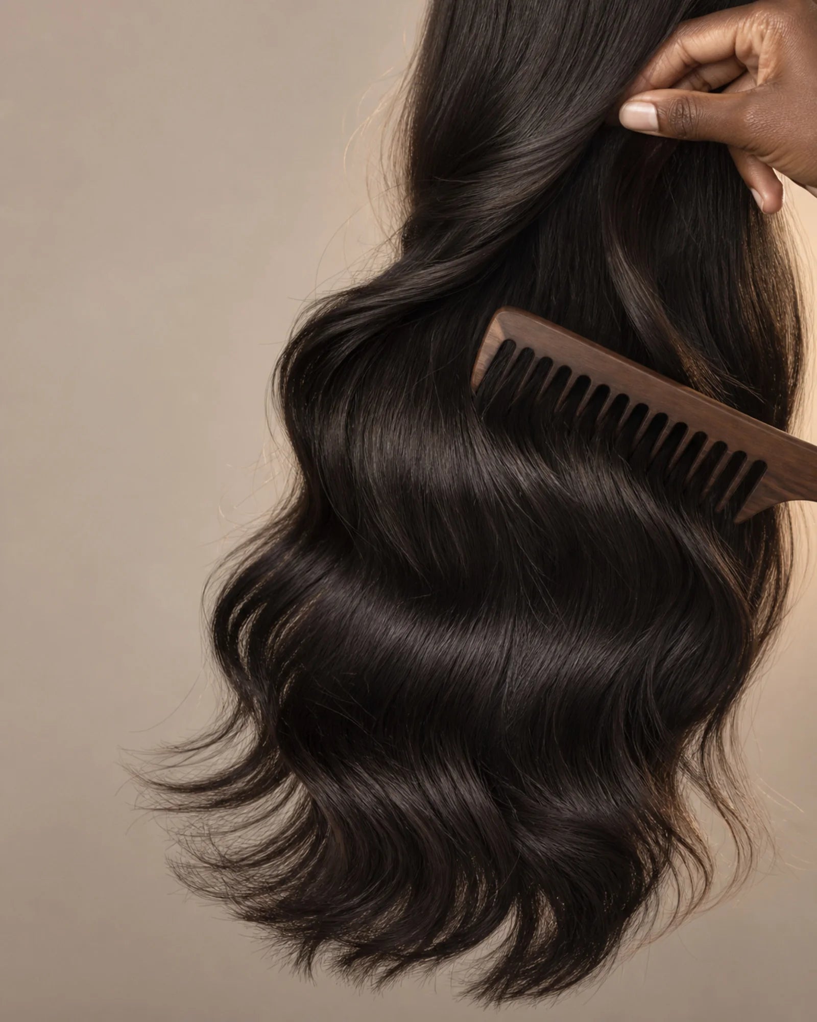Hand gently lifts and combs a long natural-black body-wave hair section to show strand texture and full ends.