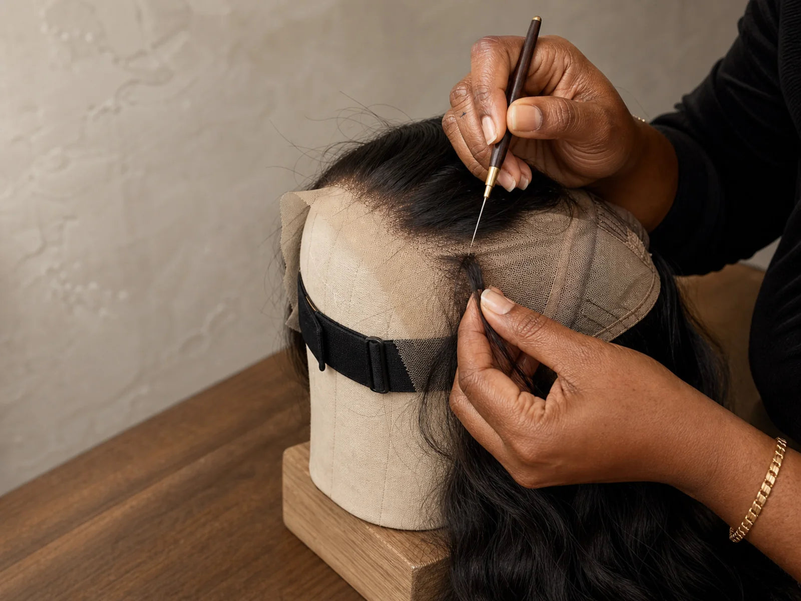 Close view of skilled hands building a natural-black wig on a canvas head.