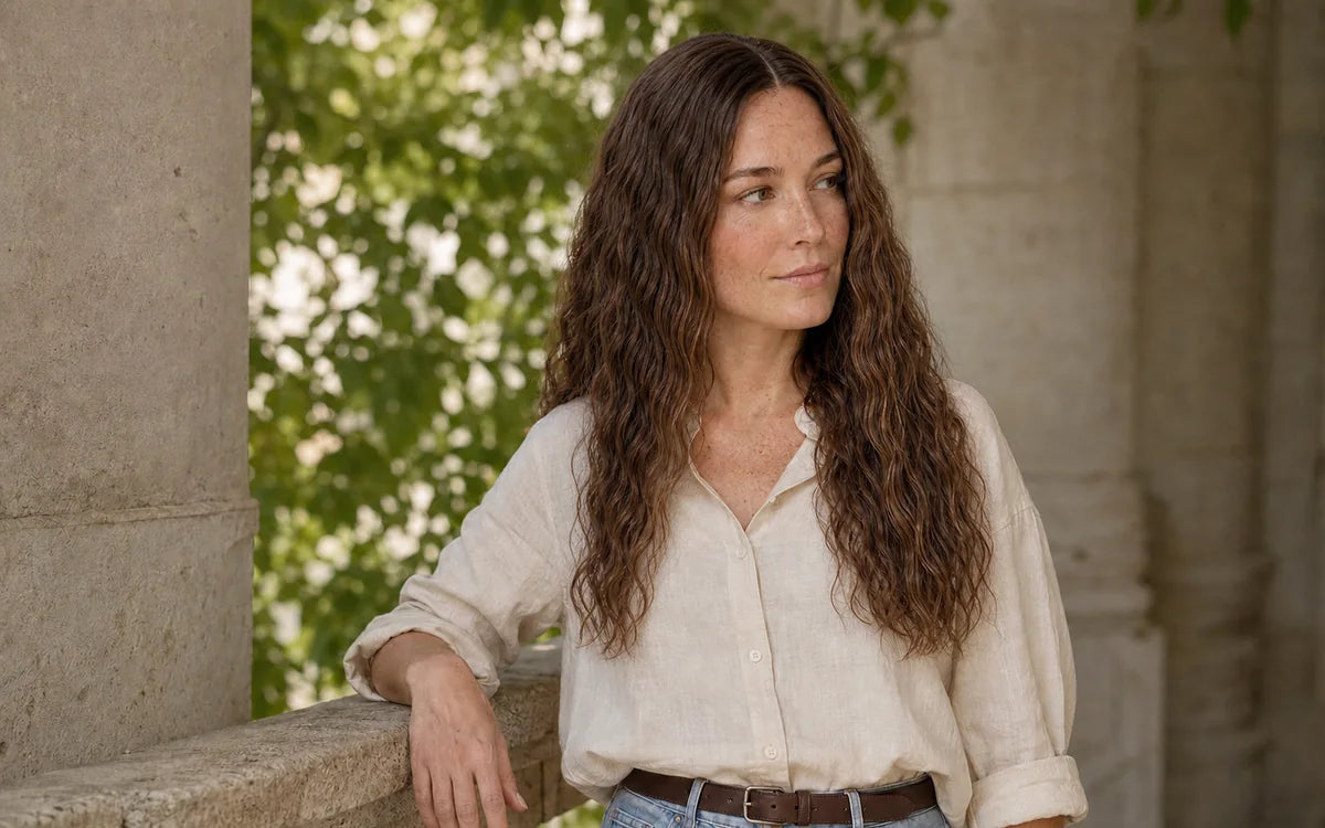 Woman with long brown wet-look waves beside a stone column and greenery.